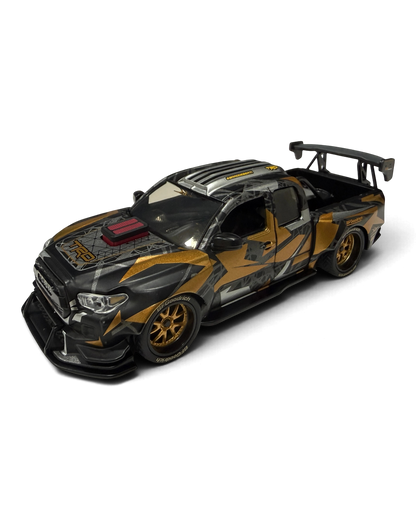 VaultifyUK Hot Wheels Premium 1:43 DeBerti Toyota Tacoma diecast truck in black, grey, and orange camo with bronze wheels