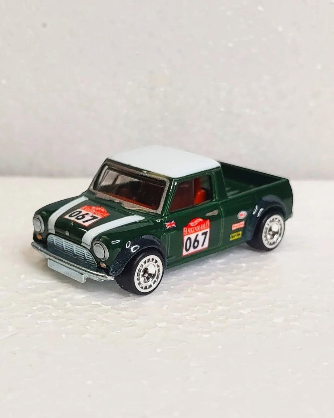 VaultifyUK Hot Wheels Premium 67 Austin Mini Pickup in green with white roof and racing decals on a white surface