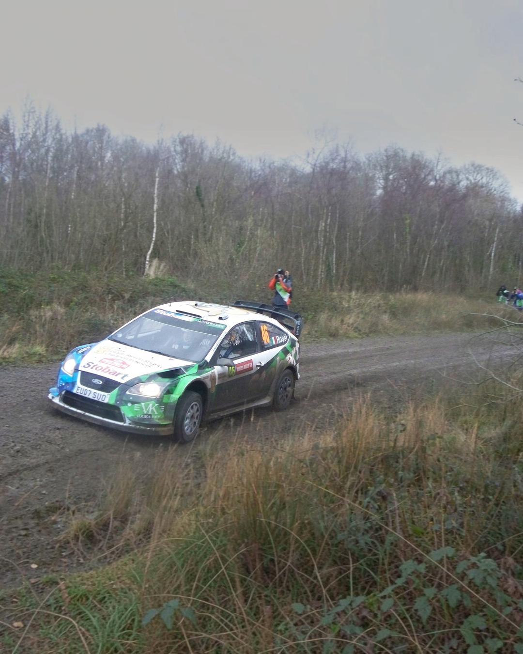 VaultifyUK Ford Focus RS WRC rally car in green and white livery driving on a dirt track through a forest