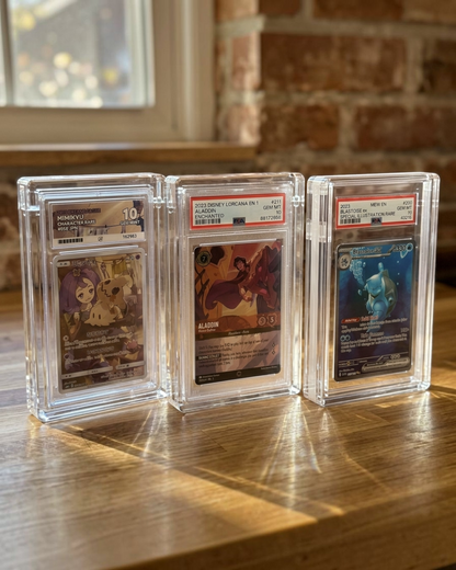VaultifyUK magnetic clear acrylic display cases holding three PSA graded trading cards standing on a wooden table.
