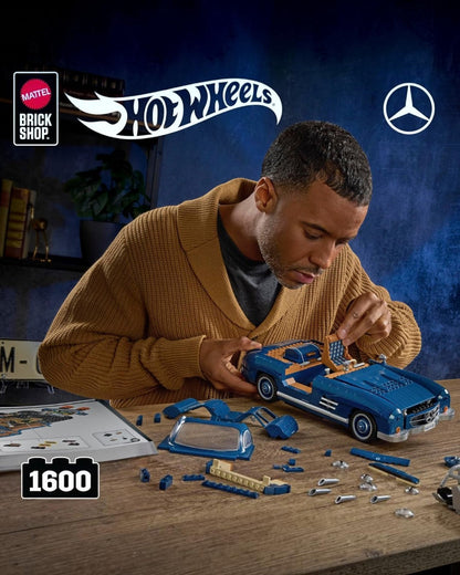 A man building a blue VaultifyUK Mattel Brick Shop Hot Wheels Mercedes-Benz 300 SL model car on a wooden desk.