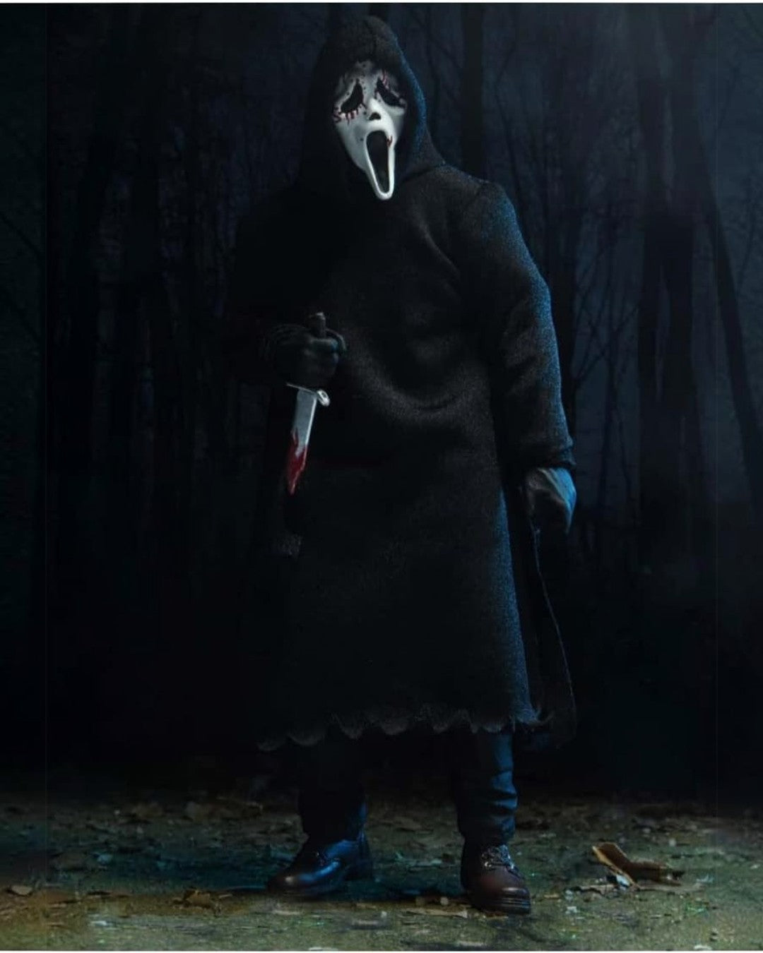 VaultifyUK NECA Ghost Face action figure wearing a fabric robe and holding a bloody knife in a dark forest setting