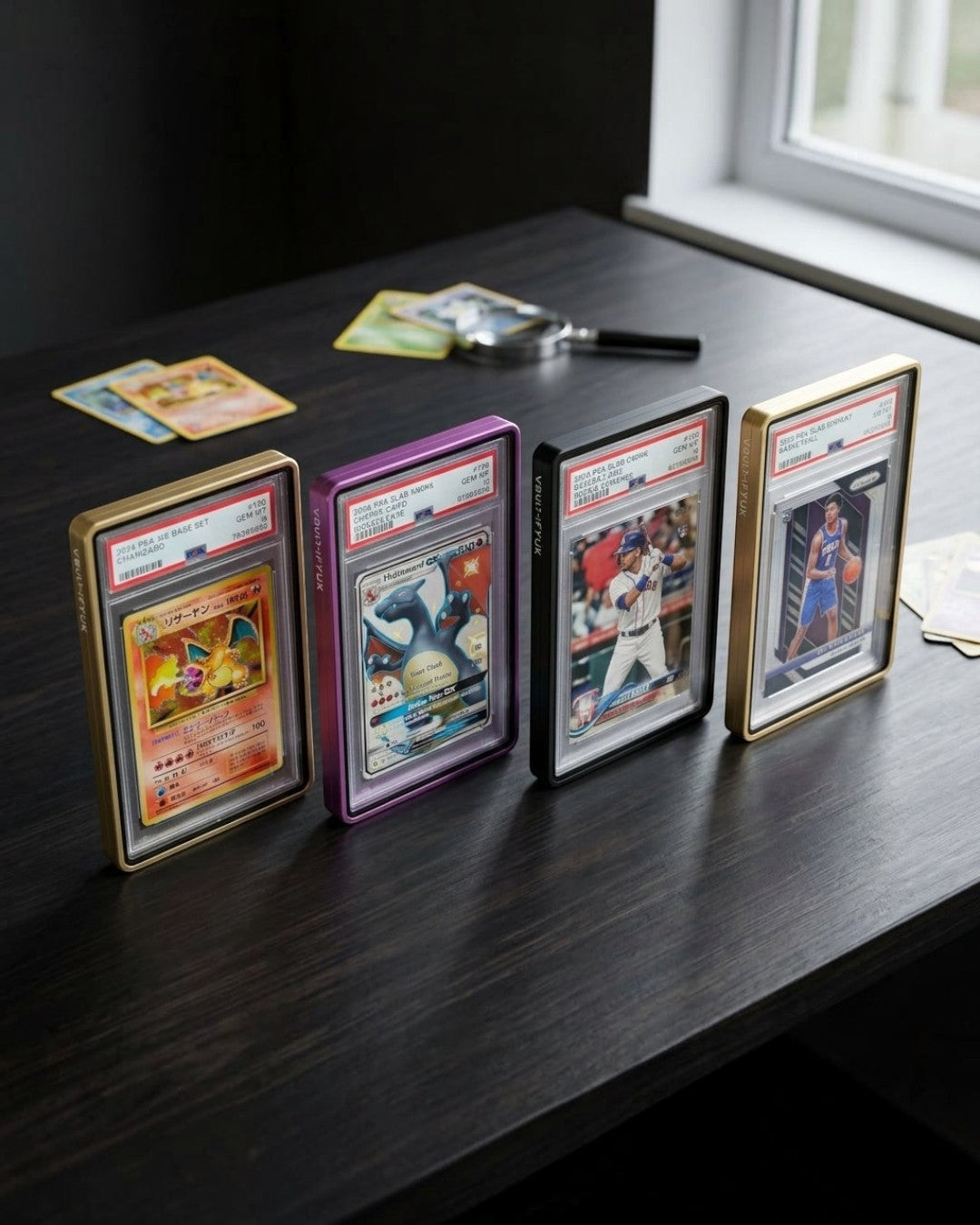 VaultifyUK Showcase aluminium PSA slab display cases in gold, purple, and black on a dark wooden desk.